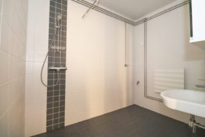 Haapaniementie 24 asunnon kylpyhuone vaaleilla seinälaatoilla ja tummilla lattialaatoilla. Haapaniementie 24 apartment bathroom with light wall tiles and dark floor tiles.