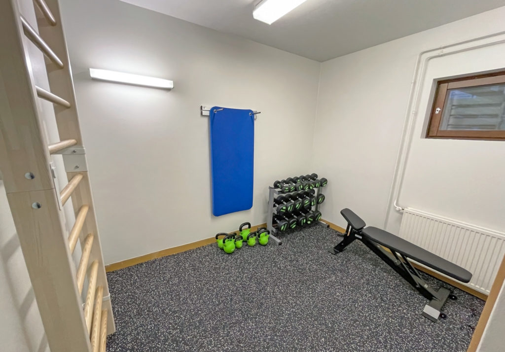 Gym at Katiskaniementie 6. Parallel bars on the left wall. Workout bench below the window on the right. At the back wall, there are exercise mats, kettlebells, and dumbbells.