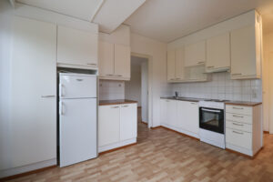 Kuopas Neulamäentie 3 asunnon vaalea keittiö, jossa on paljon kaappitilaa. Lattiat ovat puunväriset. The light-colored kitchen of the Kuopas Neulamäentie 3 apartment has plenty of cabinet space. The floors are wood-colored.