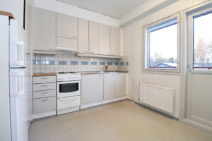 Petkelkuja 1 asunnon vaalea keittiö, jossa on vaalea muovimattolattia. Keittiöstä on pääsy parvekkeelle. Petkelkuja 1 apartment with a light-colored kitchen with light-colored plastic flooring. The kitchen has access to the balcony.